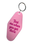 A pink motel retro keychain 'Text me when you get there' in dark pink lettering, attached to a silver metal keyring.