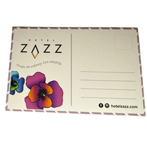 A rectangular Hotel Zazz postcard. The postcard has a white background with a thin purple border, the Hotel Zazz logo and tagline on the left, two colorful flower illustrations, and writing areas on the right.