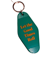 A green plastic keychain with orange text reading 'Let the Good Times Roll' on a wooden surface.