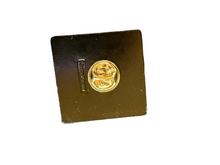 A small round silver-tone pin or badge attached to a square black backing.