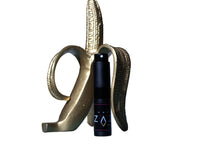 A bottle of Sweet Banana Slurpee Perfume placed inside a banana-shaped holder, with a dark background.